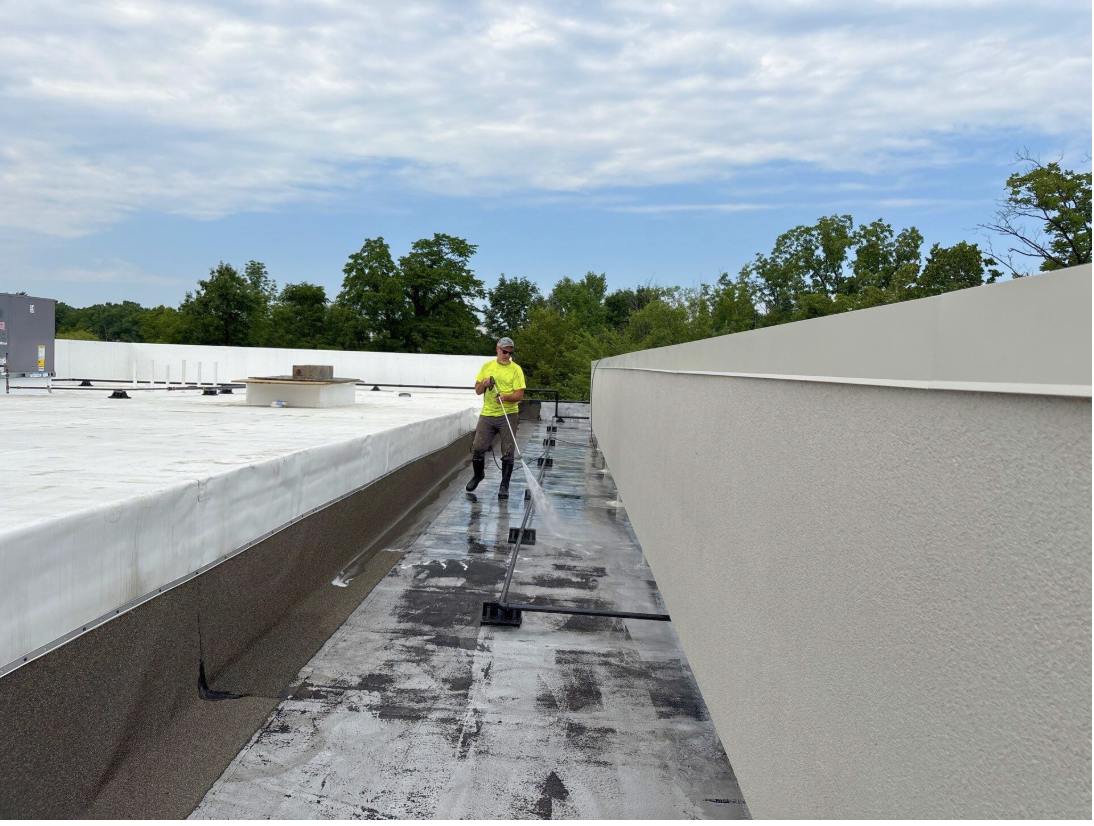 Technician cleaning flat roof membrane before commercial roof inspection checklist walkover