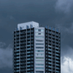 Commercial high-rise building faces threatening storm clouds highlighting the need for emergency roof damage inspections after severe weather