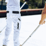 Roofing professionals applying white coating with rollers as part of routine flat roof maintenance.