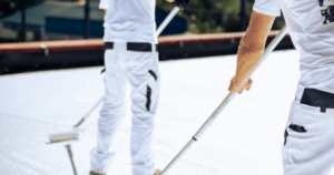 Roofing professionals applying white coating with rollers as part of routine flat roof maintenance.