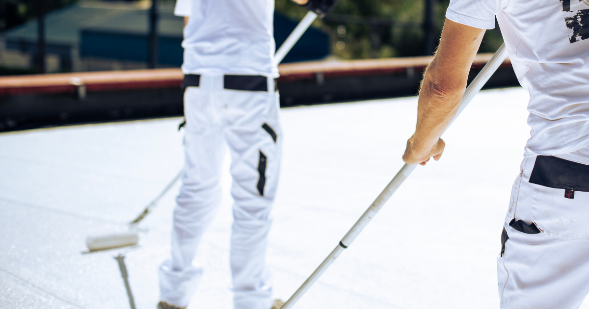 Roofing professionals applying white coating with rollers as part of routine flat roof maintenance.