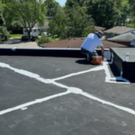 Worker applying roofing sealant on a flat commercial roof, illustrating craftsmanship and trusted roofing contractor credentials.