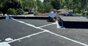 Worker applying roofing sealant on a flat commercial roof, illustrating craftsmanship and trusted roofing contractor credentials.