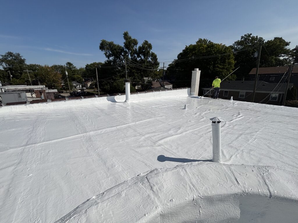 Silicone-coated commercial flat roof after restoration, technician finishing edge details.