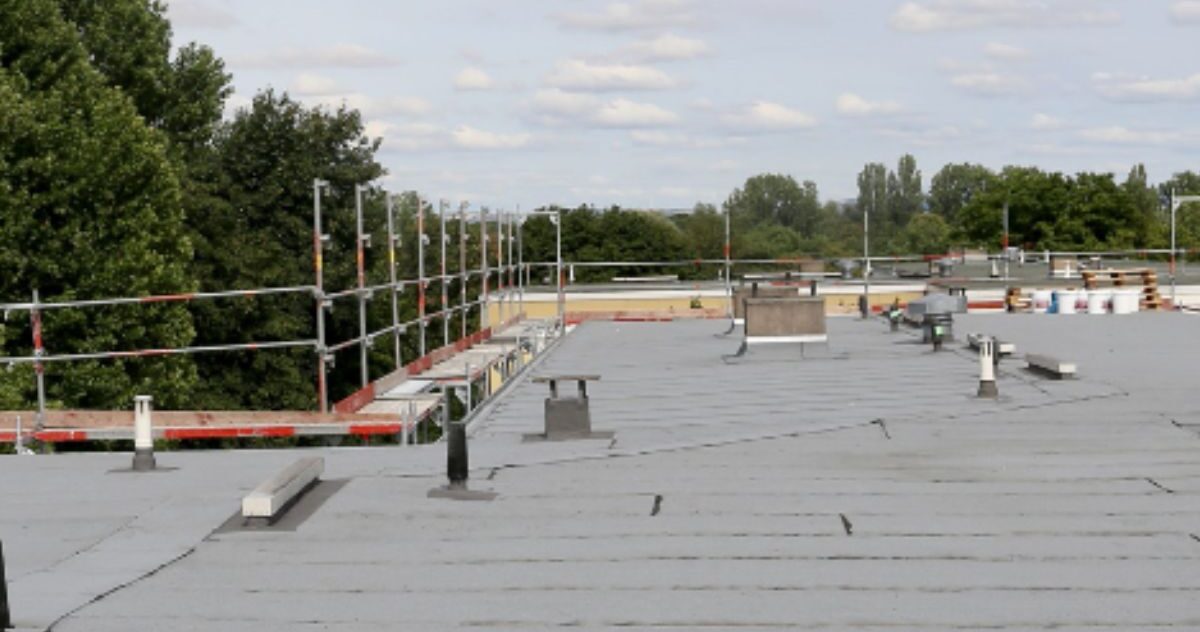 commercial roof coating contractor assessing uncoated gray flat roof before restoration