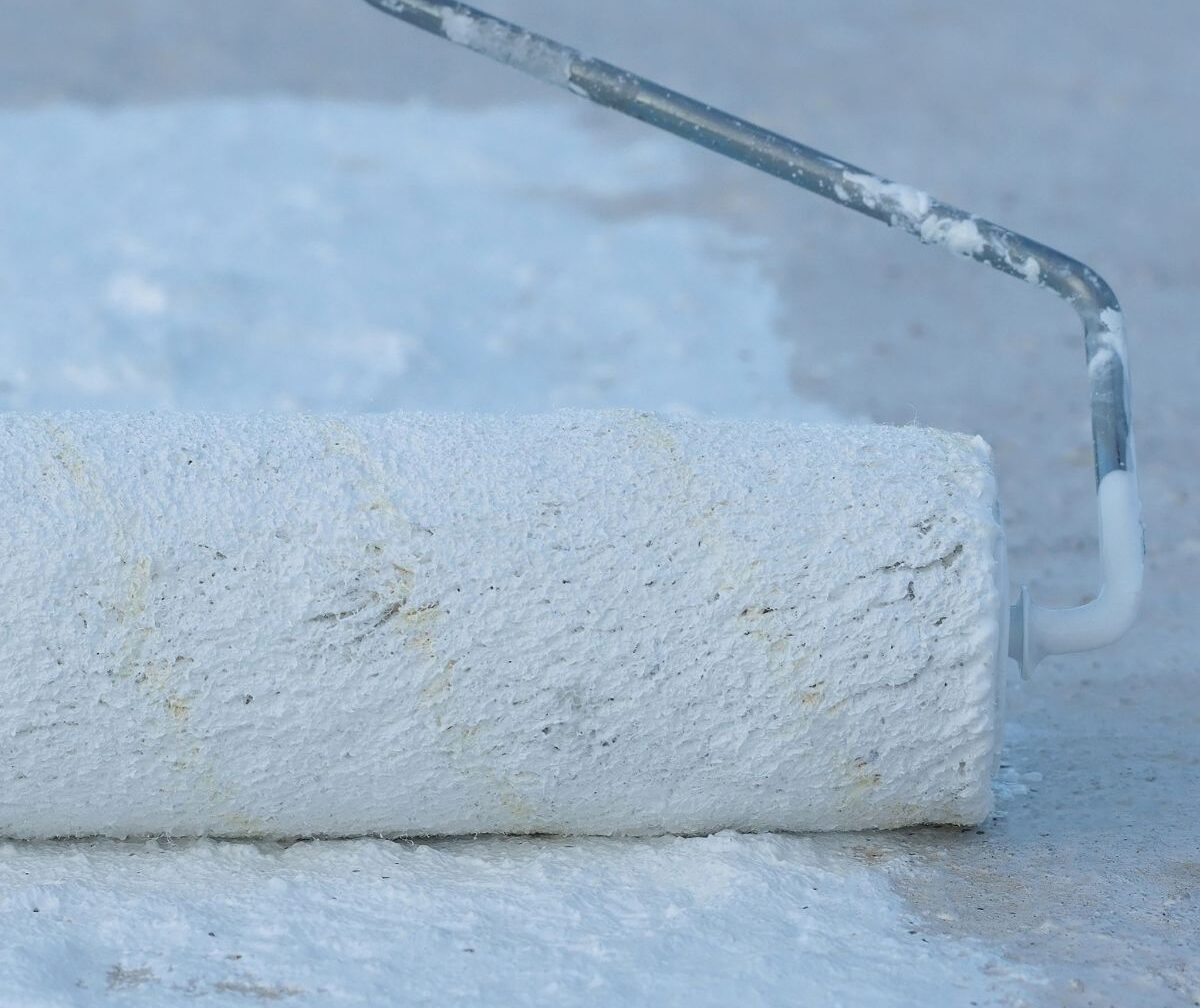 close-up of paint roller applying white silicone coating to flat roof surface during restoration