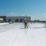 Crew applying white silicone coating on a large commercial flat roof