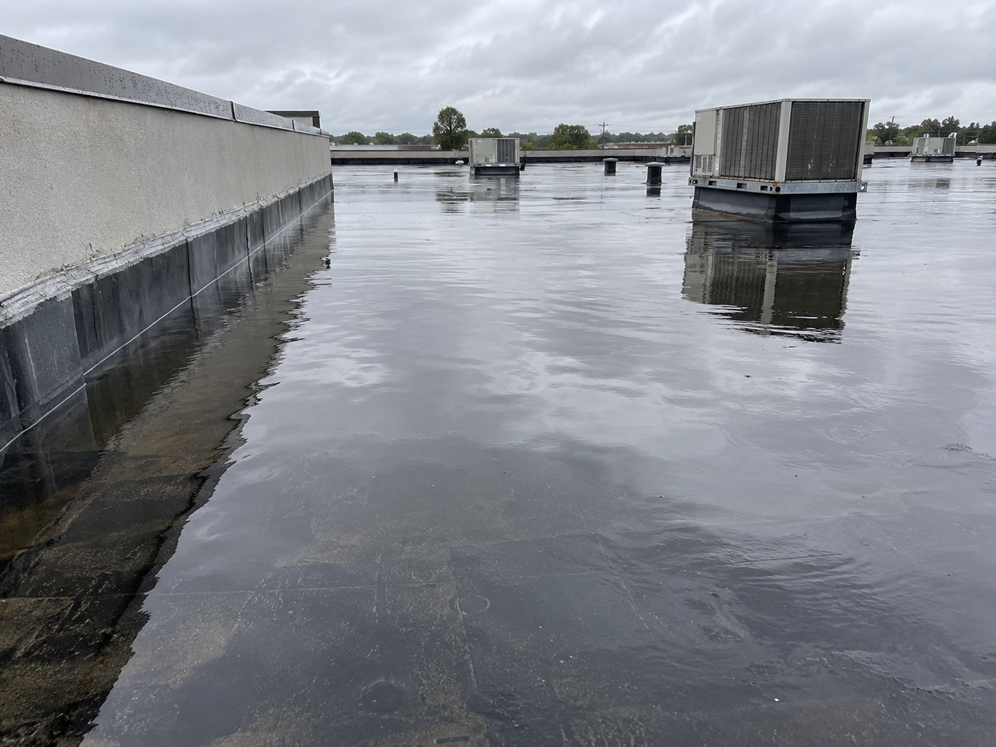 Standing water risen against base flashing on a flat commercial roof after heavy rain